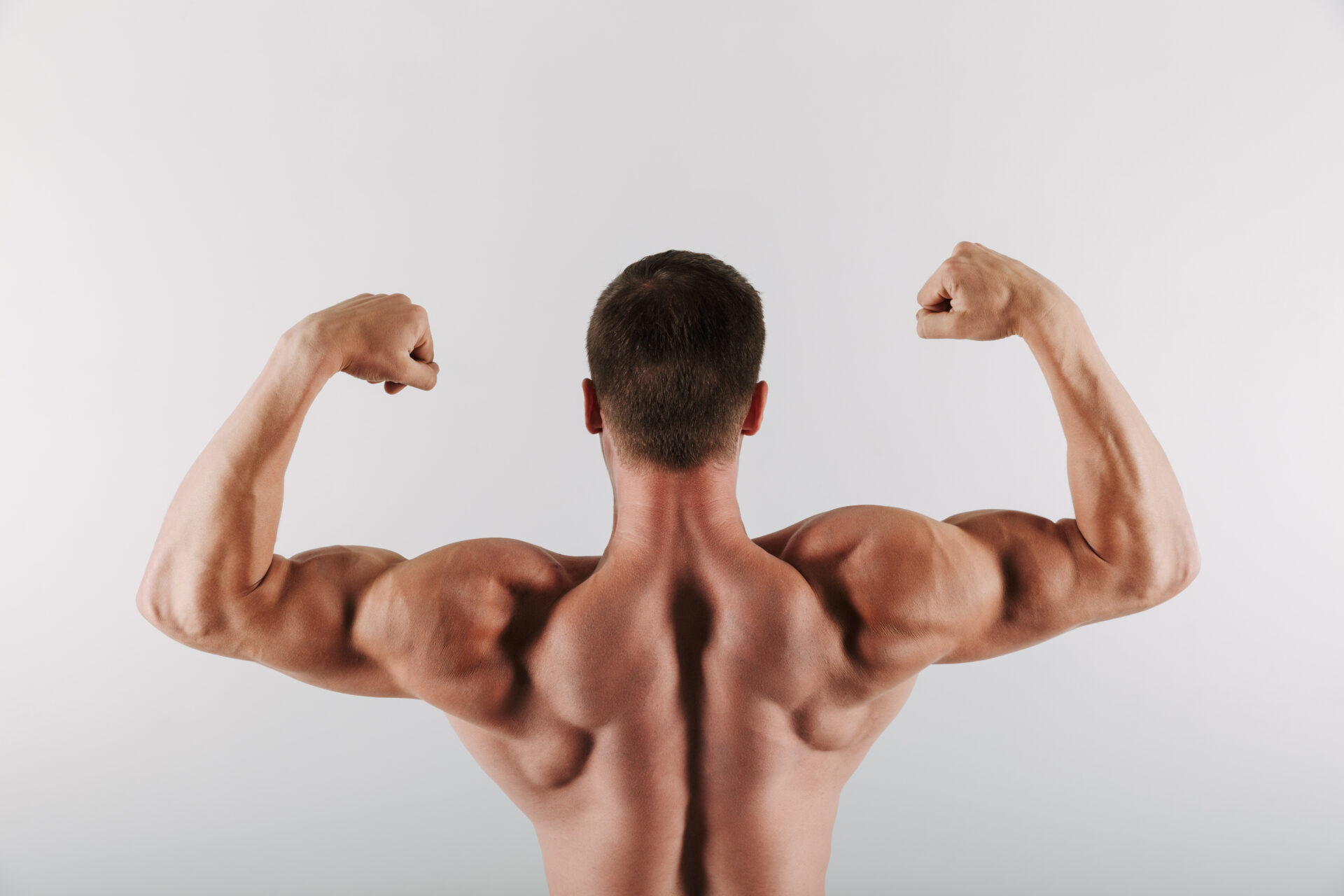 Back view photo of young sportsman standing isolated over grey background showing biceps. (Image by freepik )