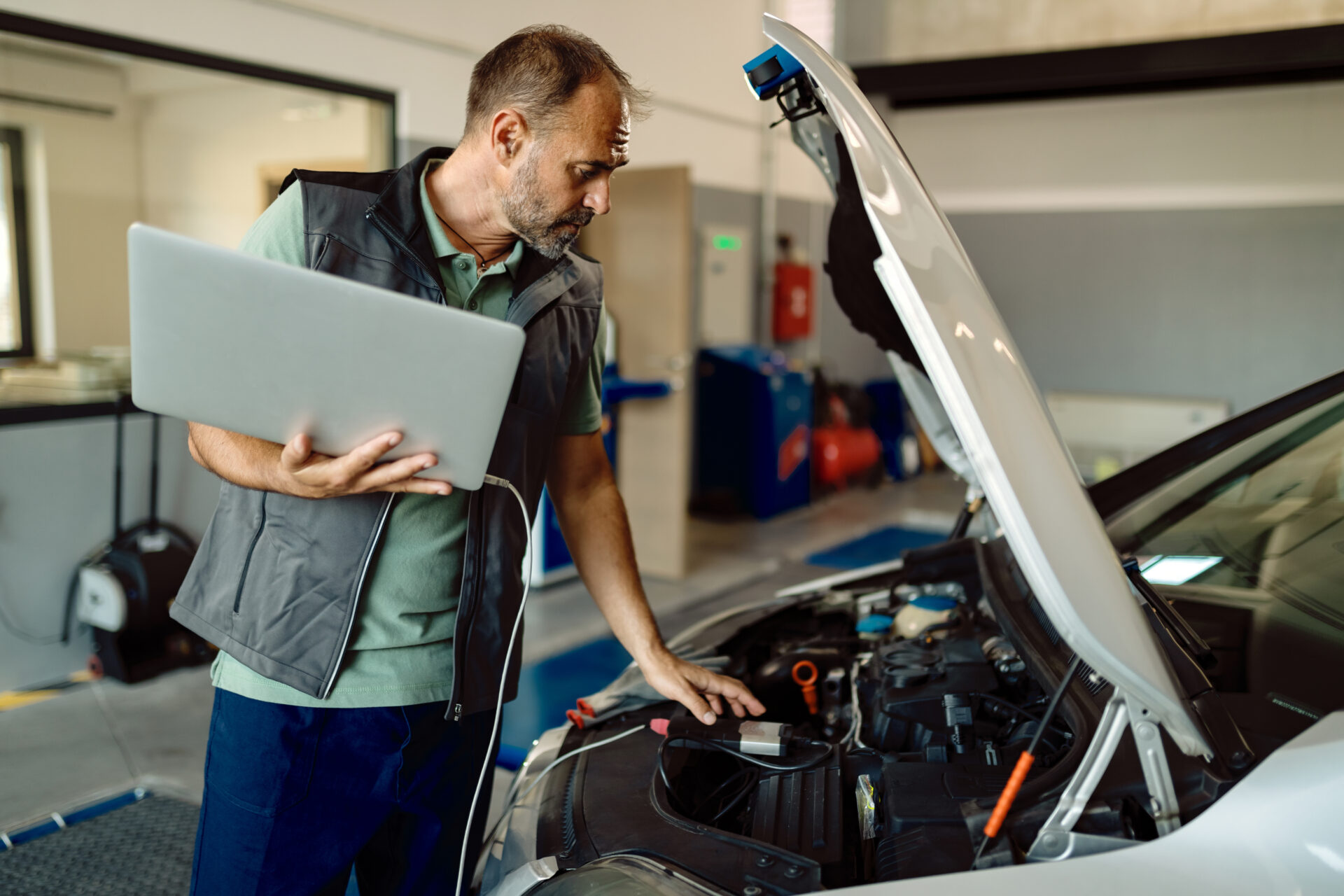 Auto repairman using laptop while examining car engine in a work (Image by freepik )